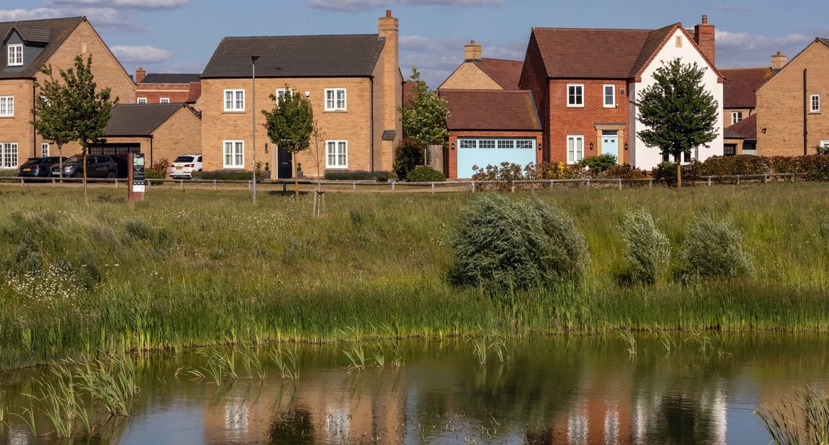 Alconbury Weald landscape featuring a lake in the foreground, with homes in the background and their reflections visible in the water.